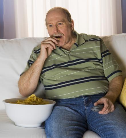 Image d'un homme regardant la télévision et mangeant des chips, exemple de comportement sédentaire