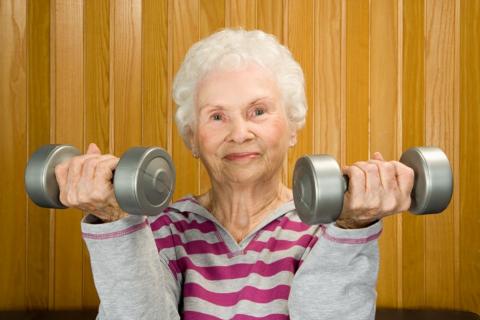 Starsza kobieta, która ćwiczy mięśnie ramion używając małych ciężarków